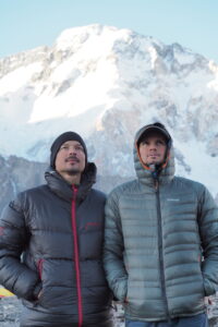 Młodzi mężczyzni w zimowych kurtkach pozują na tle ośnieżonej góry.