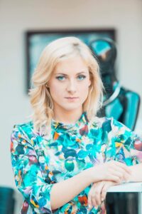Katarzyna Guran, sopranistka, młoda blondynka, półdługie rozpuszczone włosy, błękitne oczy, sukienka w błękitny wzór.