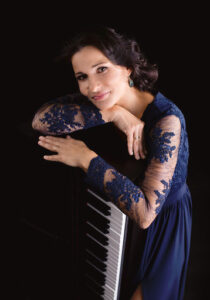 Pianistka Joanna Błażej Łukasik, młoda brunetka, półdługie rozpuszczone włosy, granatowa koronkowa sukienka. Opiera się o klawiaturę keyboarda.