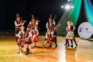 Dorośli muzycy i grupka dzieci w krakowskich strojach ludowych podczas występu.