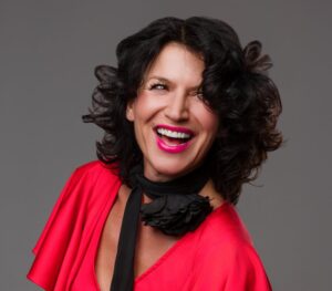 Uśmiechnięta kobieta, burza czarnych włosów, czerwona sukienka, czarna apaszka.