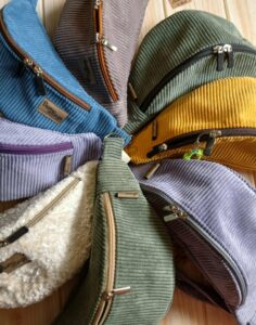 Zdjęcie przedstawia małe damskie torebki z zamkiem tzw. nerki, każda w innym kolorze, wykonane ze sztruksu i innych materiałów